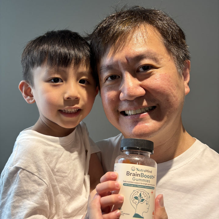 A father and his young son smiling together, holding a bottle of BrainBoost+ gummies